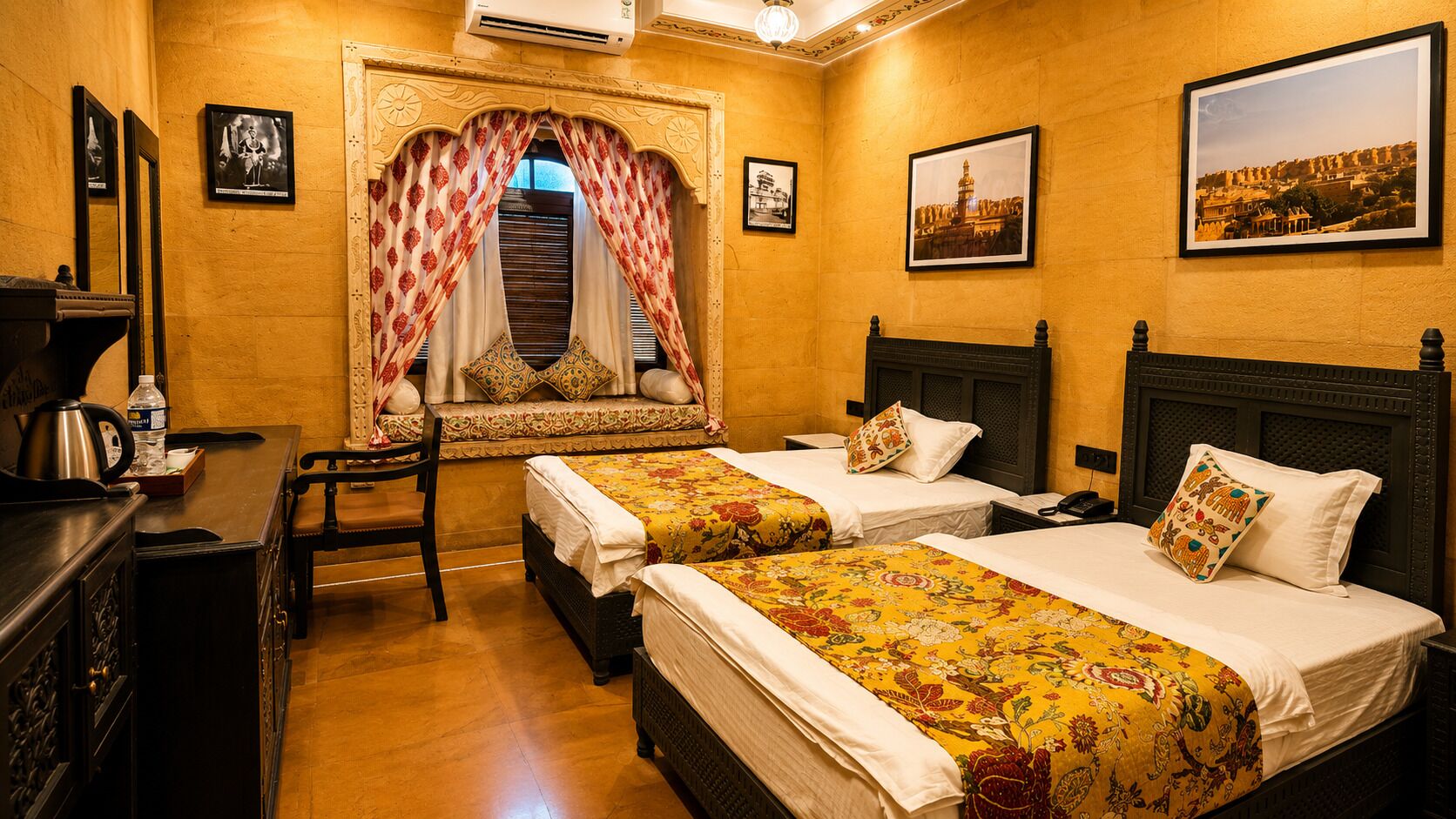 Una camera d'albergo con due letti, una zona salotto con una poltrona, un tavolino con un bollitore e quadri appesi alle pareti.