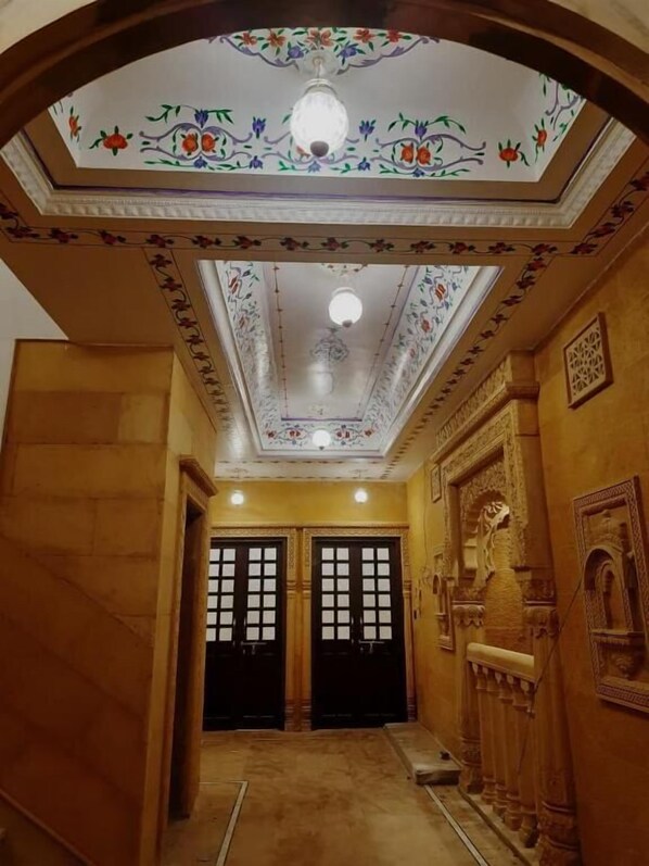 An interior hallway with ornate ceiling decorations, double doors, and a patterned floor.