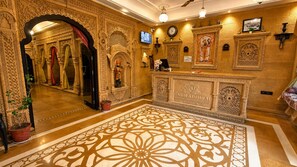 An ornate reception area with intricate wall carvings, a large patterned carpet, and a clock on the wall.