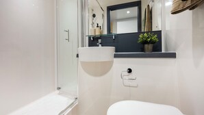 Et moderne badeværelse med et glasbadeværelsesafskærmning, en hvid vask og et spejl over vasken.