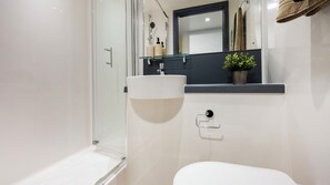 Ein modernes Badezimmer mit Duschkabine aus Glas, einem weißen Waschbecken und einem Spiegel darüber.