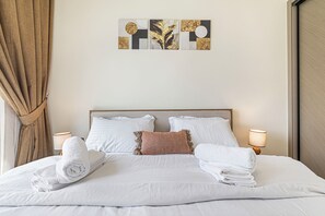 Een opgemaakt bed met witte lakens, een hoofdbord en twee bedlampjes.