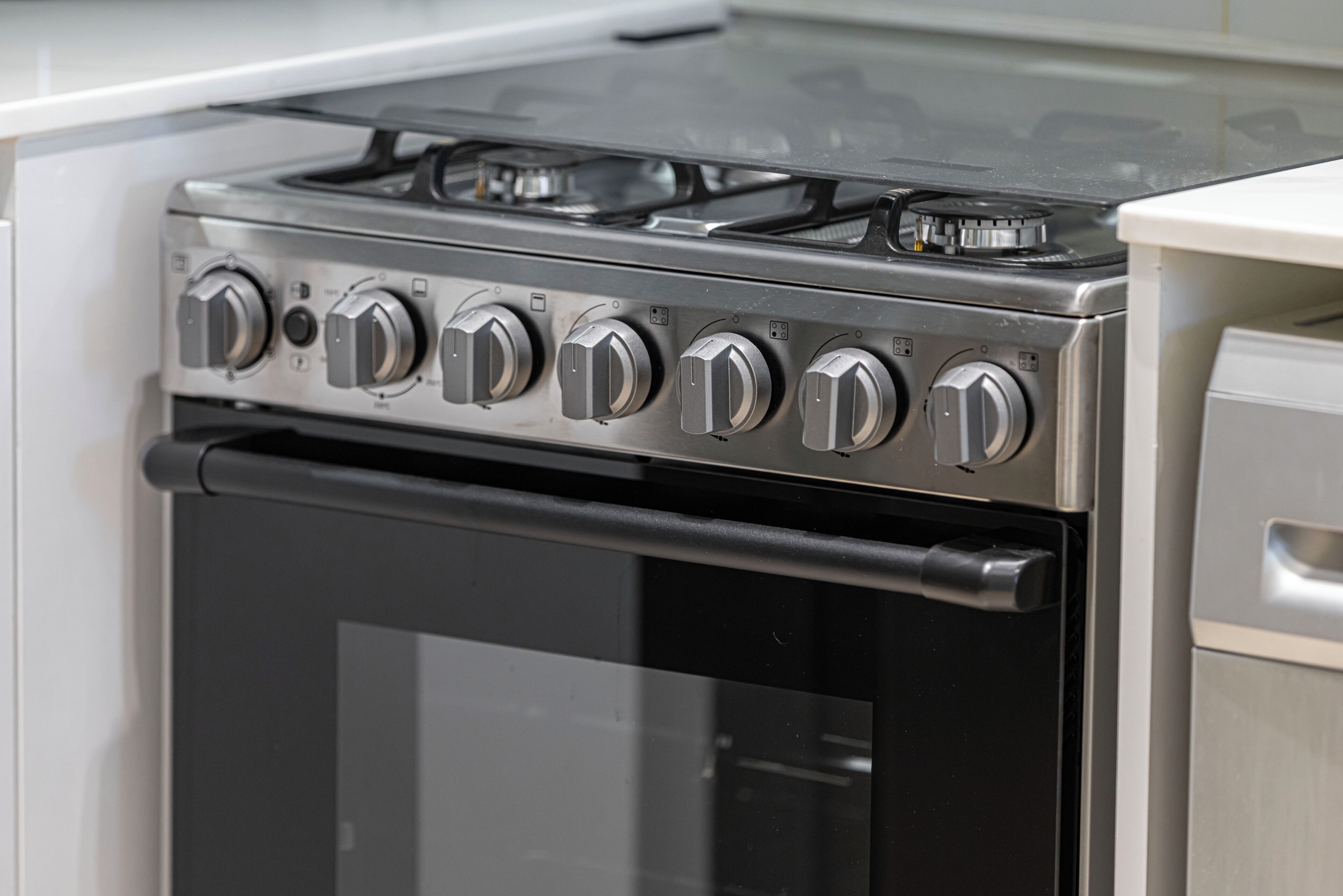 A stainless steel range with six knobs, a black oven door, and a white countertop.