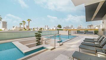 Un espace piscine aménagé sur le toit, offrant une vue sur les toits de la ville, avec des chaises longues et un petit palmier.
