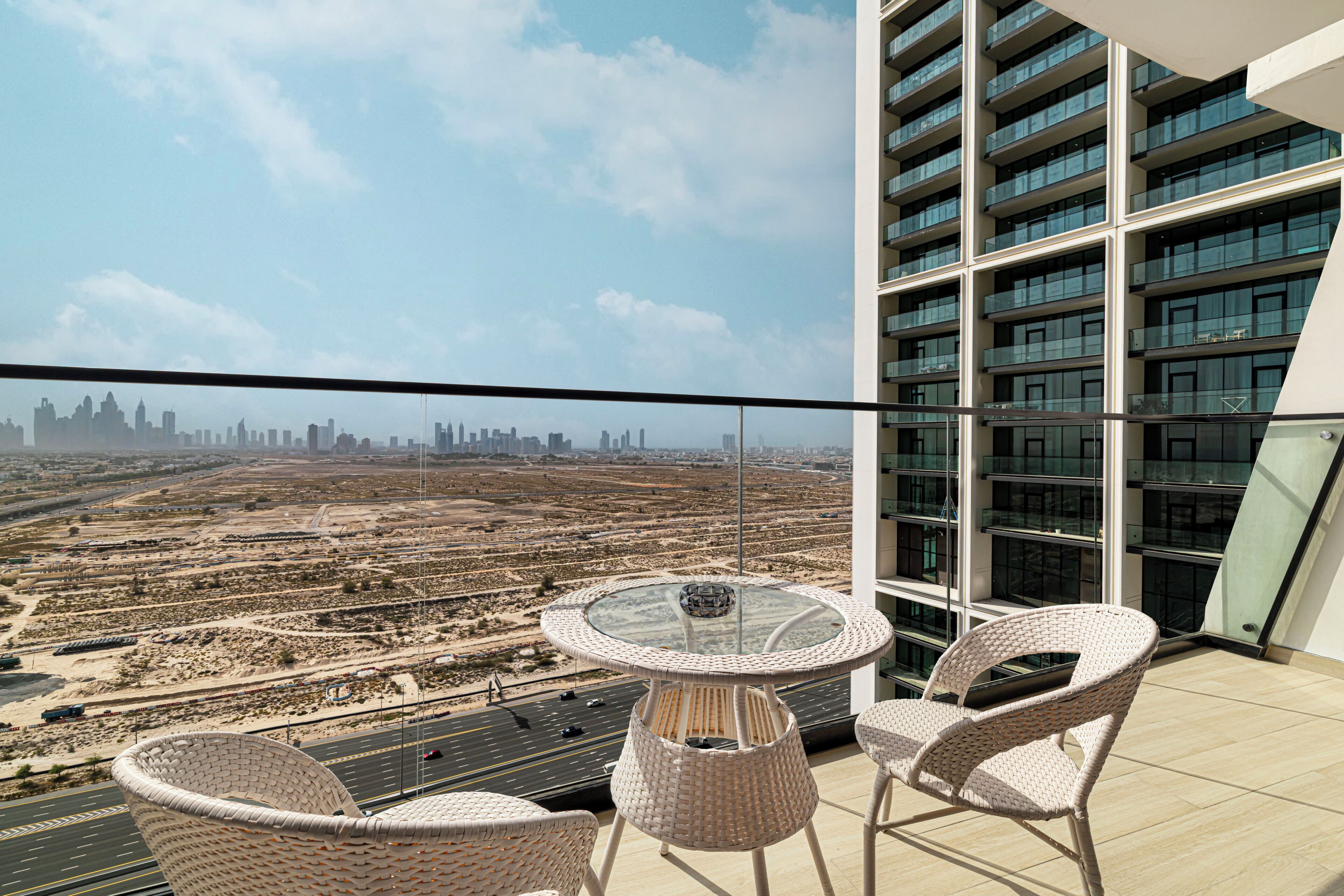 Un balcon avec des fauteuils en osier et une table en verre, offrant une vue sur le paysage urbain.
