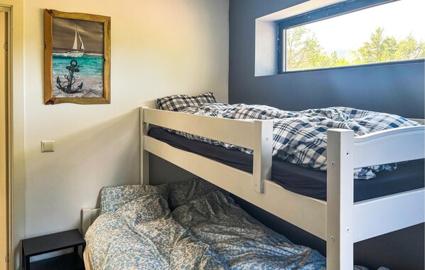 A bunk bed room with a window, a painting, and a small table.