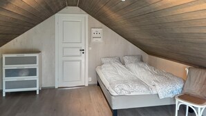 A bedroom with a sloped ceiling, a bed with patterned bedding, a white dresser, and a chair. - Nice home in Hellandsjøen with WiFi (Hellandsjøen)