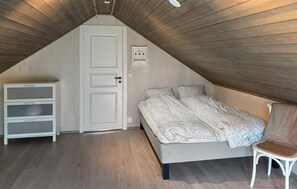 A bedroom with a sloped ceiling, a bed with patterned bedding, a white dresser, and a chair. - Nice home in Hellandsjøen with WiFi (Hellandsjøen)