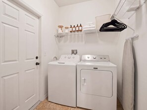 Une buanderie équipée de deux machines à laver blanches, d’un étendoir et d’une étagère où sont rangées des bouteilles et des serviettes.