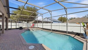 Une piscine extérieure couverte, dotée d’une terrasse en briques, d’un fauteuil de relaxation rouge et d’une clôture blanche.