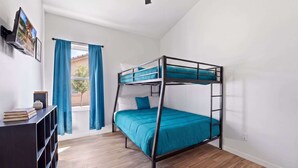Un lit superposé avec un matelas bleu, un plancher en bois, un ventilateur de plafond et une fenêtre avec des rideaux.