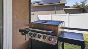 Un barbecue en acier inoxydable doté de quatre brûleurs, installé sur un balcon offrant une vue sur un quartier résidentiel et délimité par une clôture blanche.