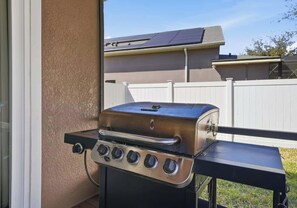 Ein Grill aus Edelstahl mit vier Brennern, platziert auf einem Balkon mit Blick auf eine Wohngegend und einen weißen Zaun.