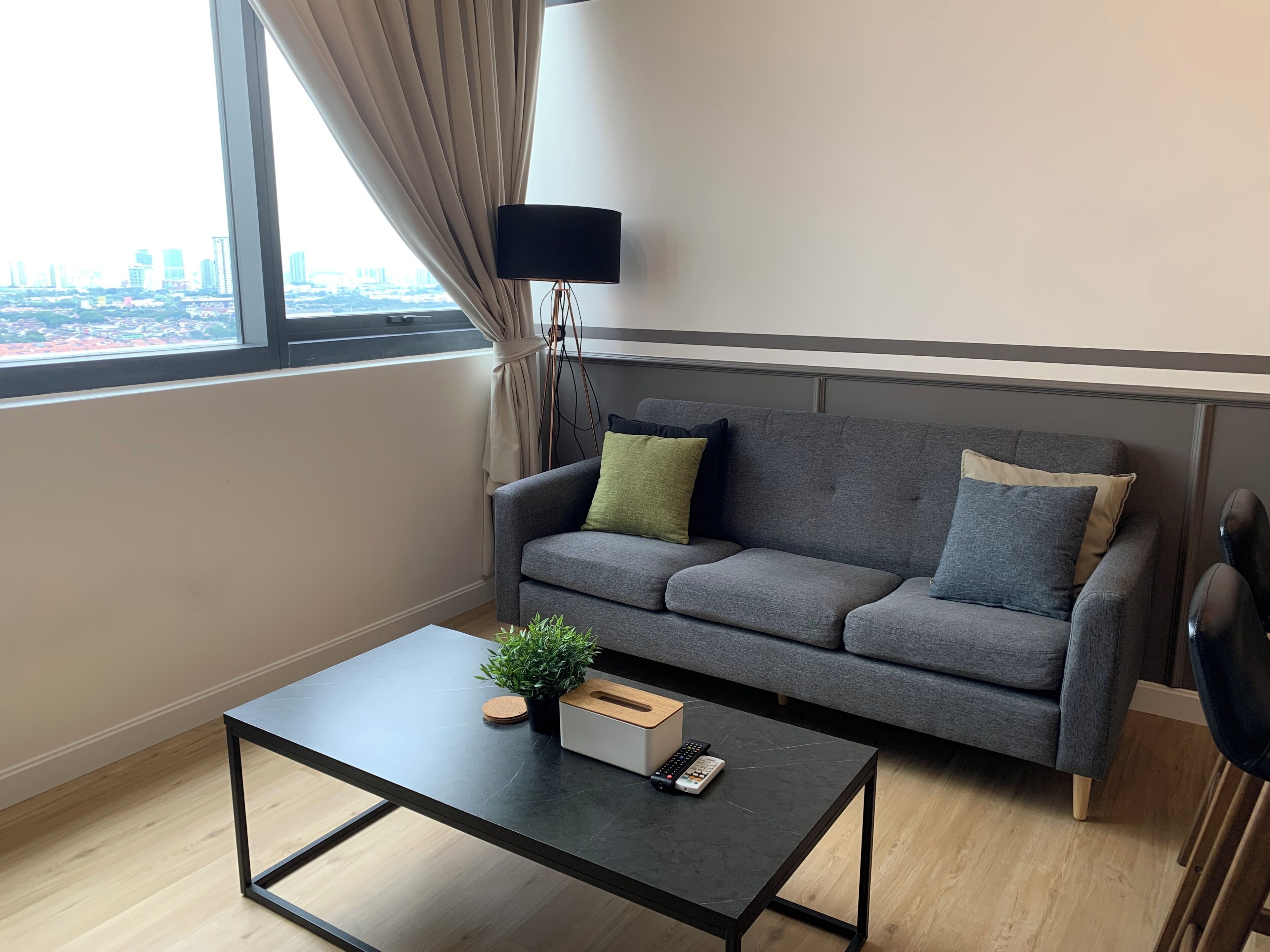 Een moderne woonkamer met een grijze bank, een zwarte salontafel en uitzicht op de stad.