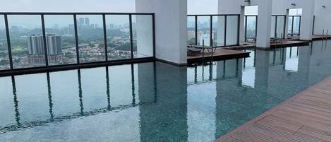 An indoor infinity pool with clear water, surrounded by a wooden deck and large windows offering a city view.