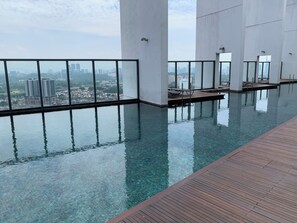 Piscina infinita interior con agua cristalina, rodeada por una terraza de madera y grandes ventanales con vistas a la ciudad.