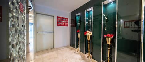 Un hall de hotel con piso de baldosas, una mesa de recepción y un separador de vidrio con un letrero rojo.