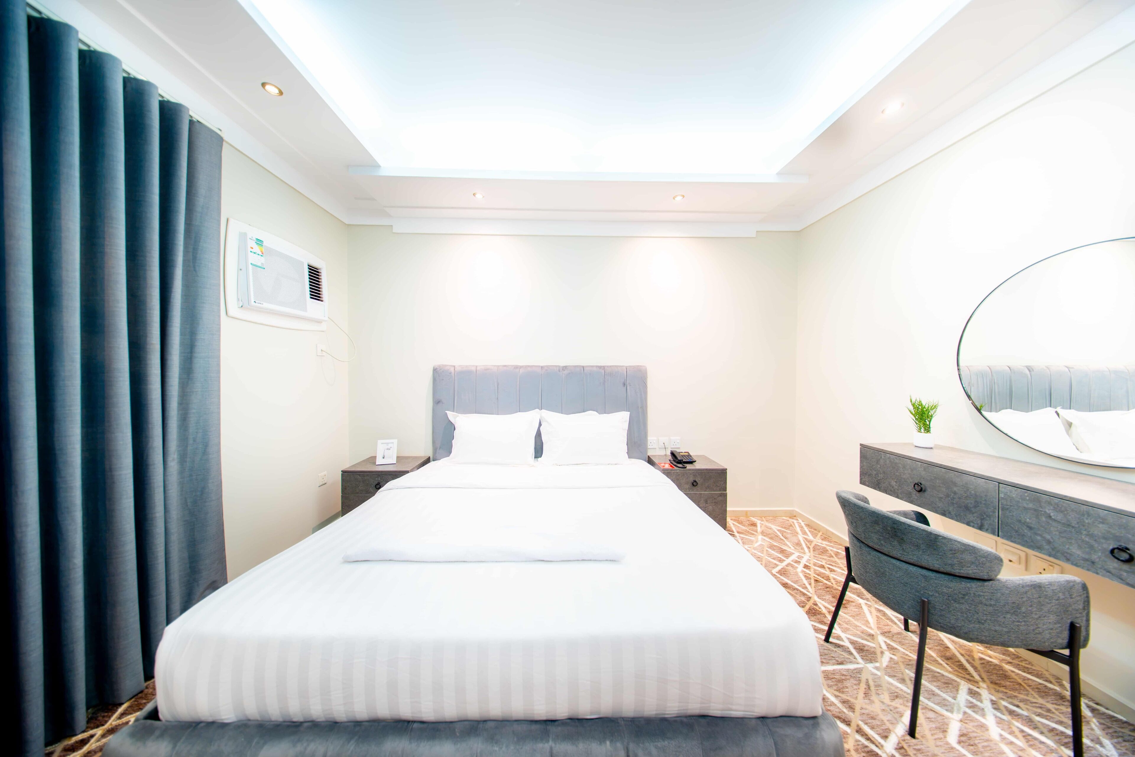 A hotel room with a large bed, a bedside table with a phone, a mirror, and a chair.