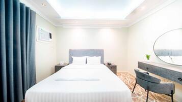 A hotel room with a large bed, a bedside table with a phone, a mirror, and a chair.