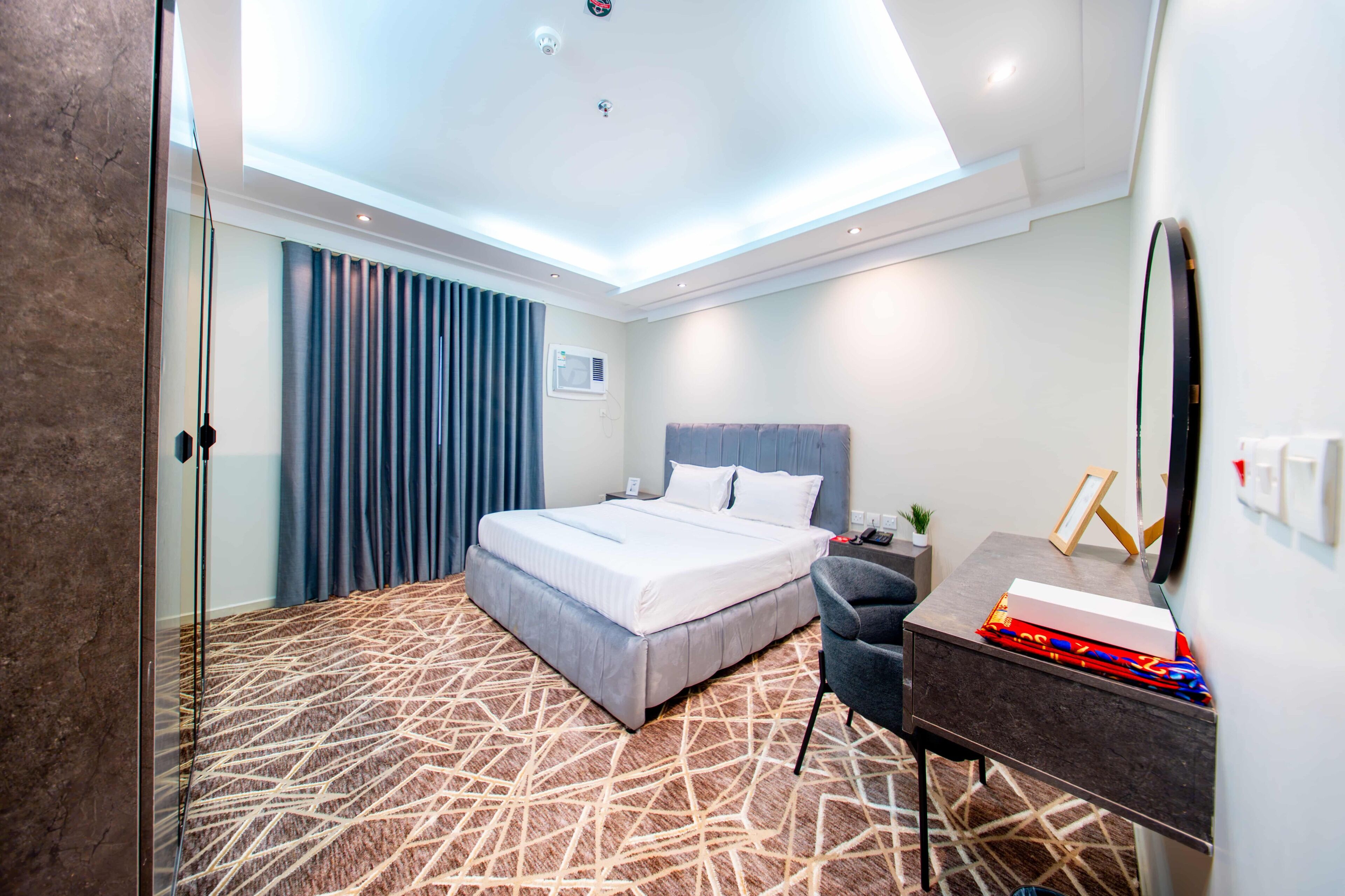 A hotel room with a bed, a desk, a chair, a mirror, and a window with curtains.