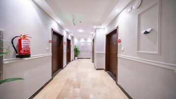 A hotel hallway with doors, a fire extinguisher, and a potted plant.