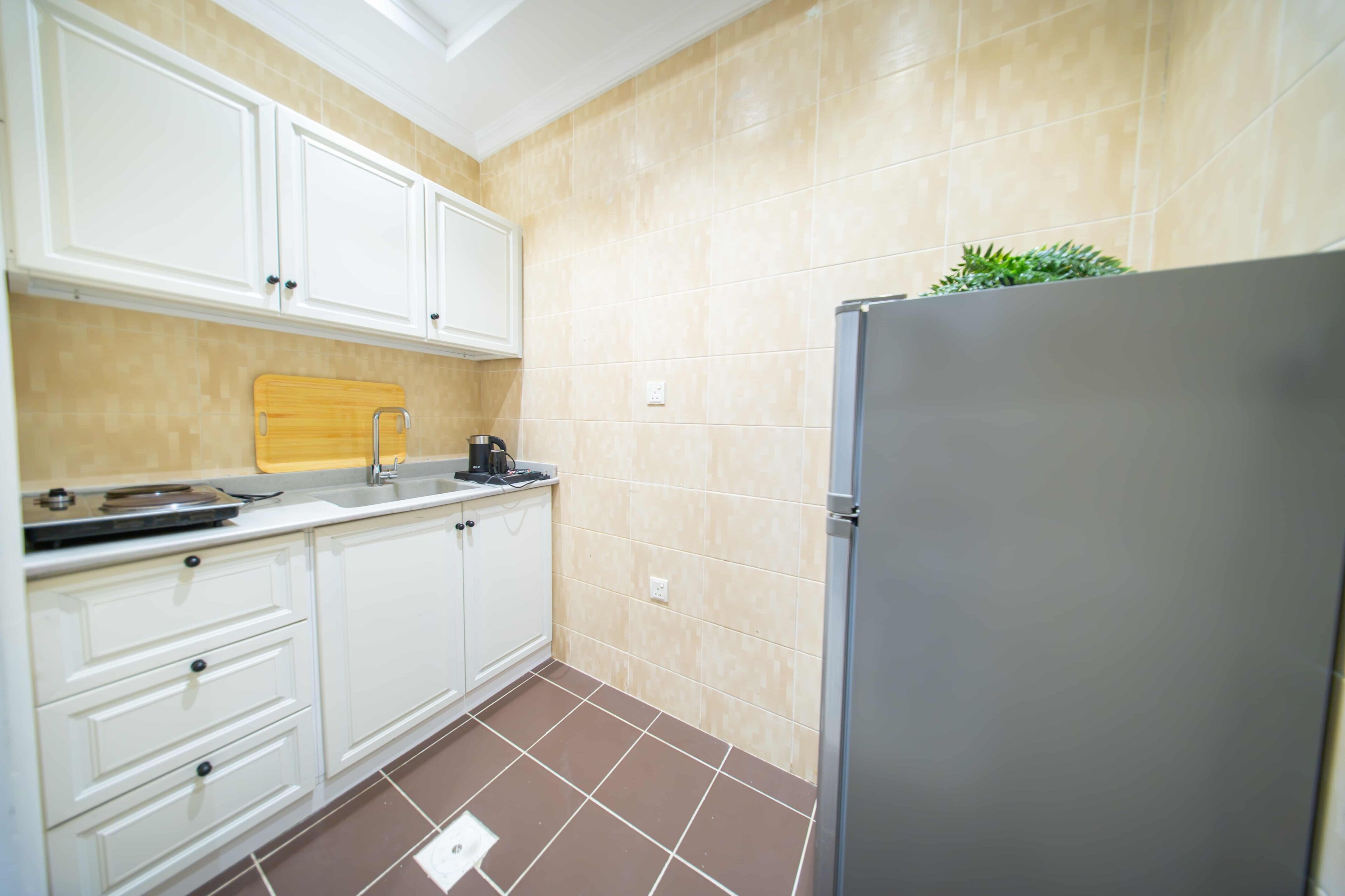 A kitchen with white cabinets, a stainless steel refrigerator, a wooden cutting board, and a sink.