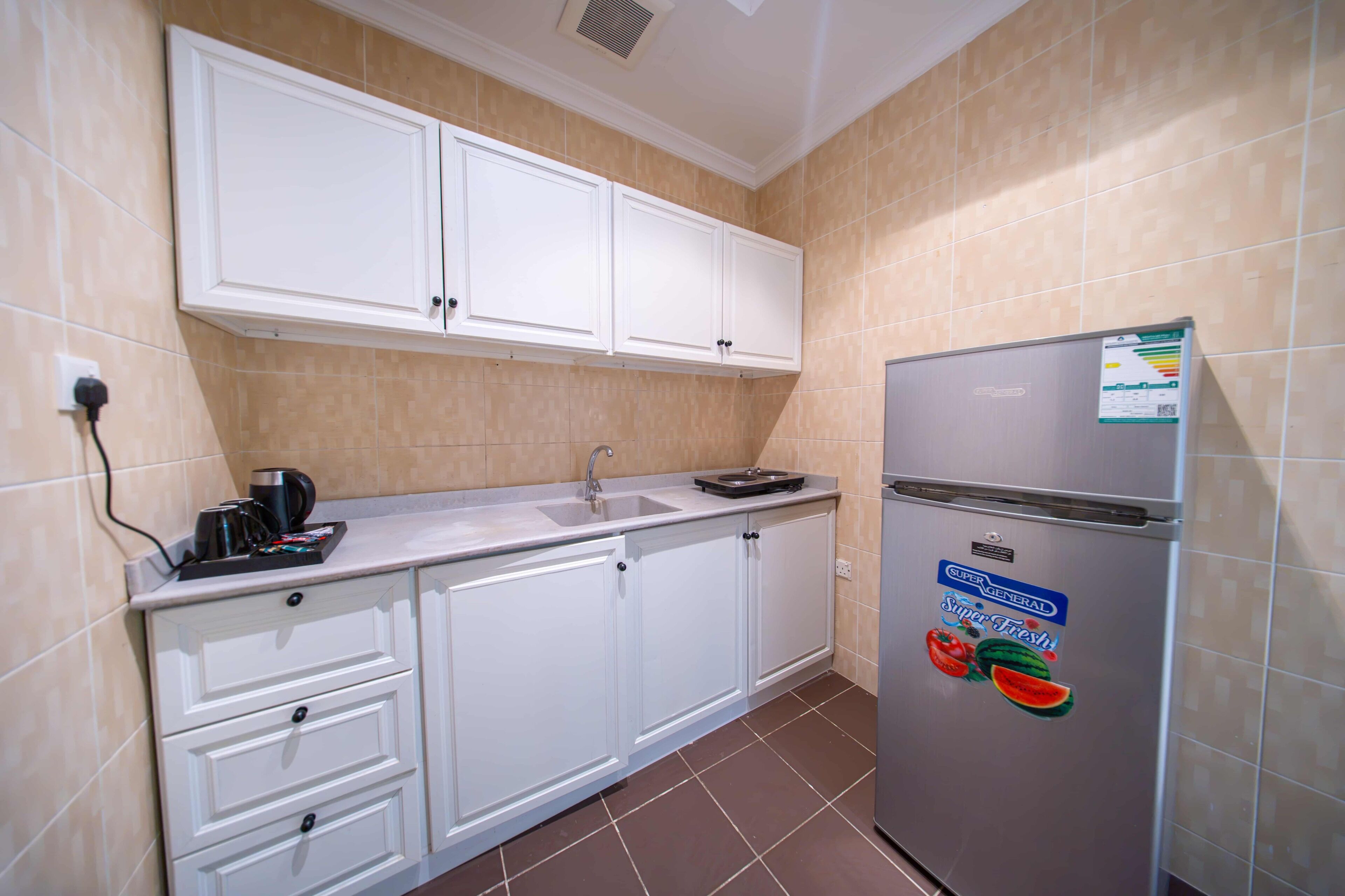 A kitchen with white cabinets, a stainless steel refrigerator, a sink, and a countertop with a coffee maker.