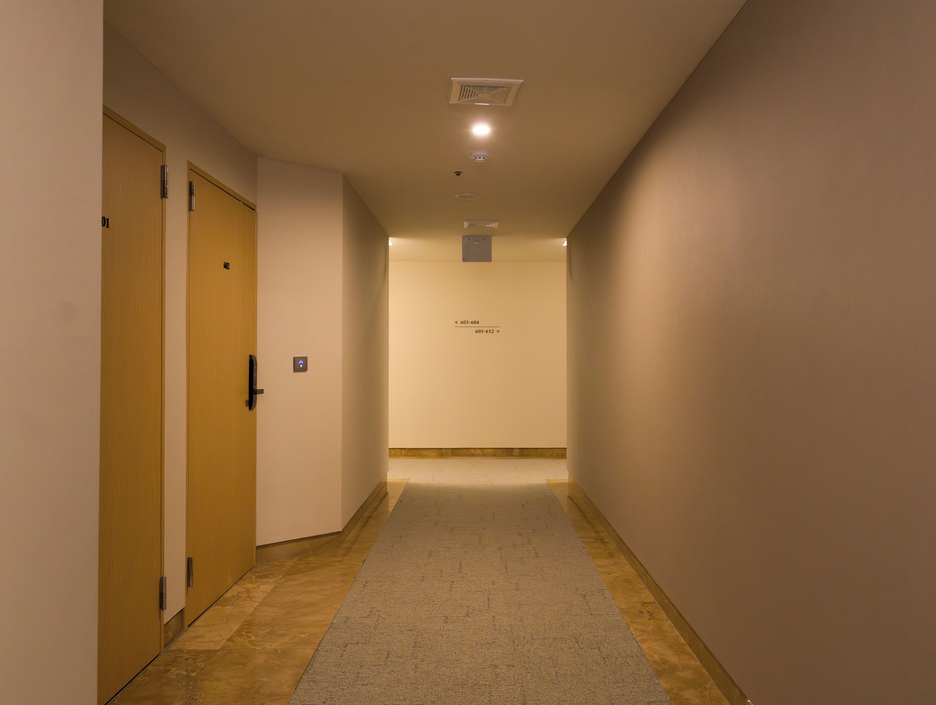 Un couloir doté d’un revêtement de sol en moquette, de portes en bois et d’un panneau mural indiquant les numéros des pièces.