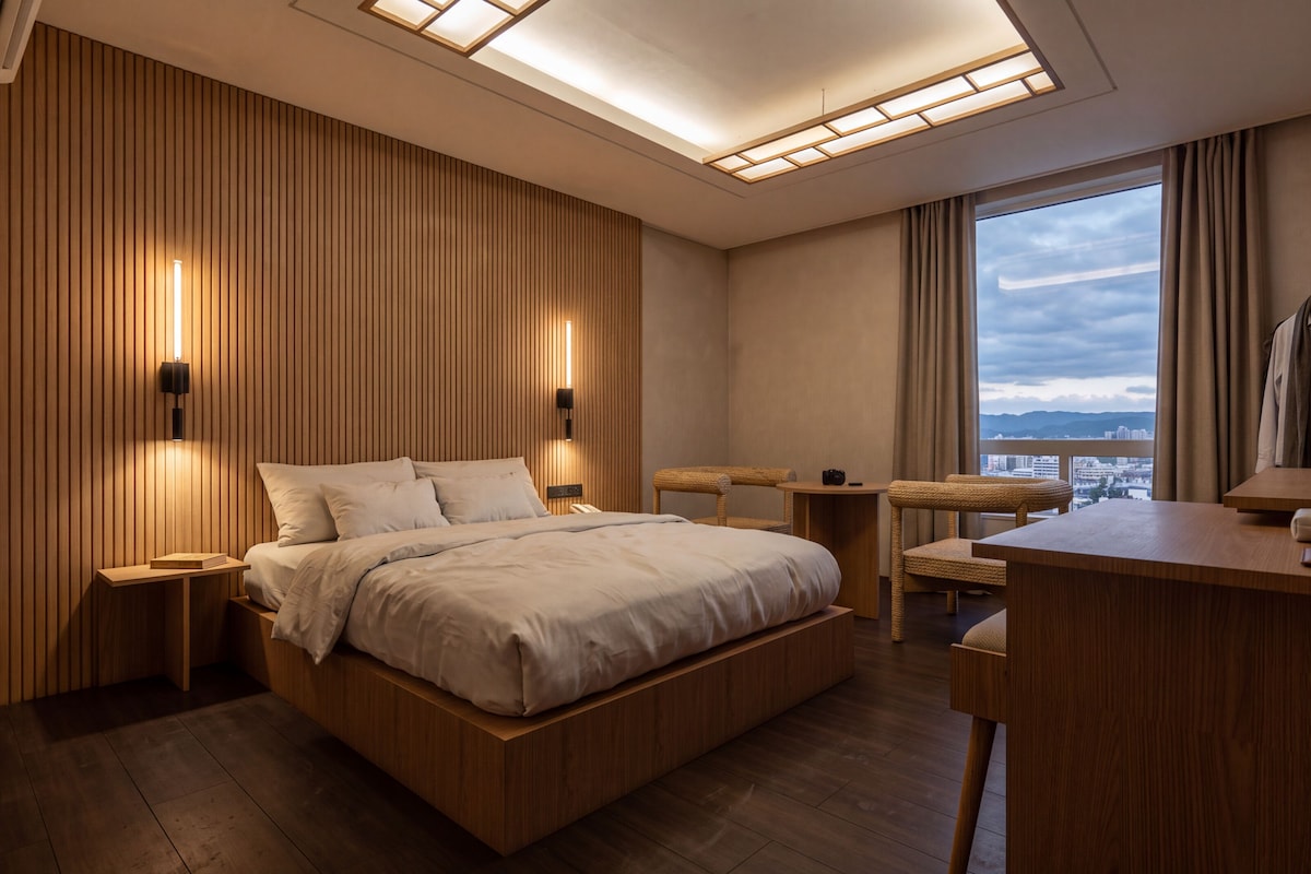 A modern hotel room with a large bed, a desk, and a view of the city.