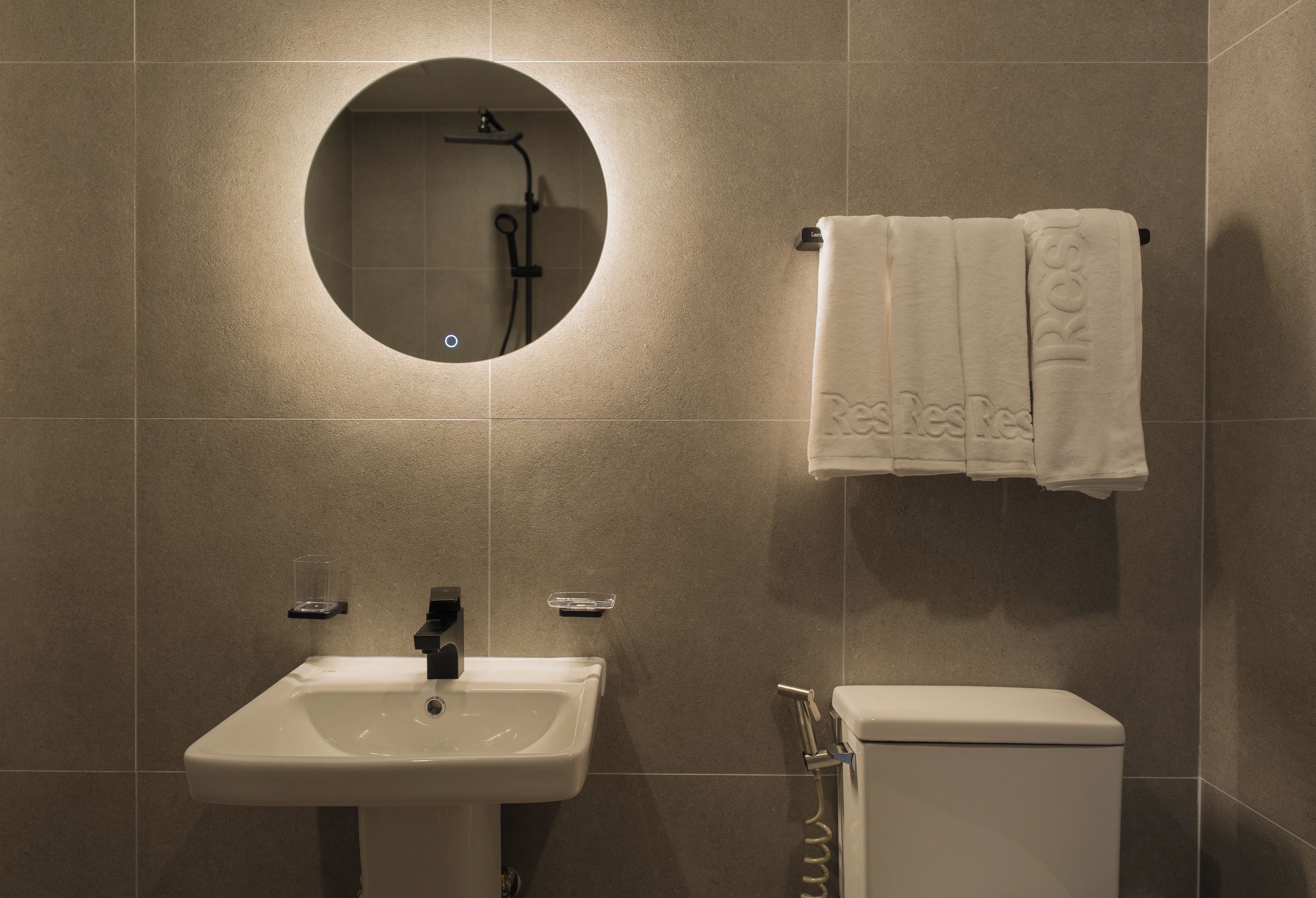 A bathroom with a round mirror, a sink, a toilet, and a towel rack with a towel.