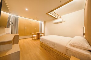 Habitación de hotel con cama, escritorio, silla, armario y aire acondicionado.