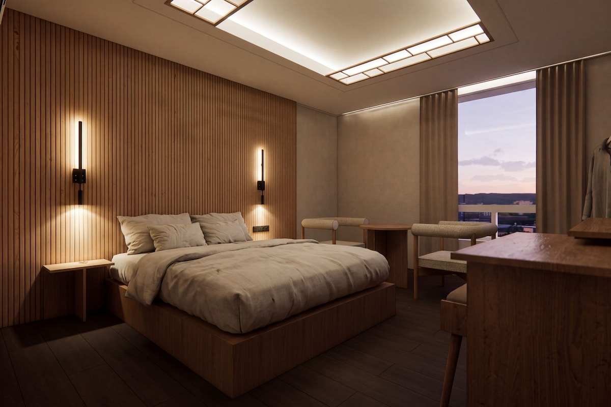 A modern hotel room with a wooden panel wall, a large bed, a desk, and a view of the city.