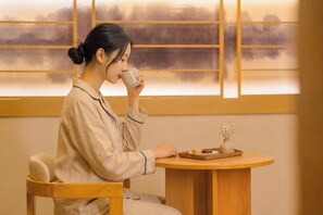 Una persona sentada en una mesa de madera con una taza y un pequeño florero con flores.