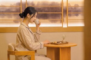 A person seated at a wooden table with a cup and a small vase with flowers.