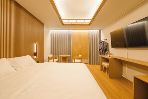 Habitación de hotel con una cama grande, un escritorio, una silla, un televisor y un armario.