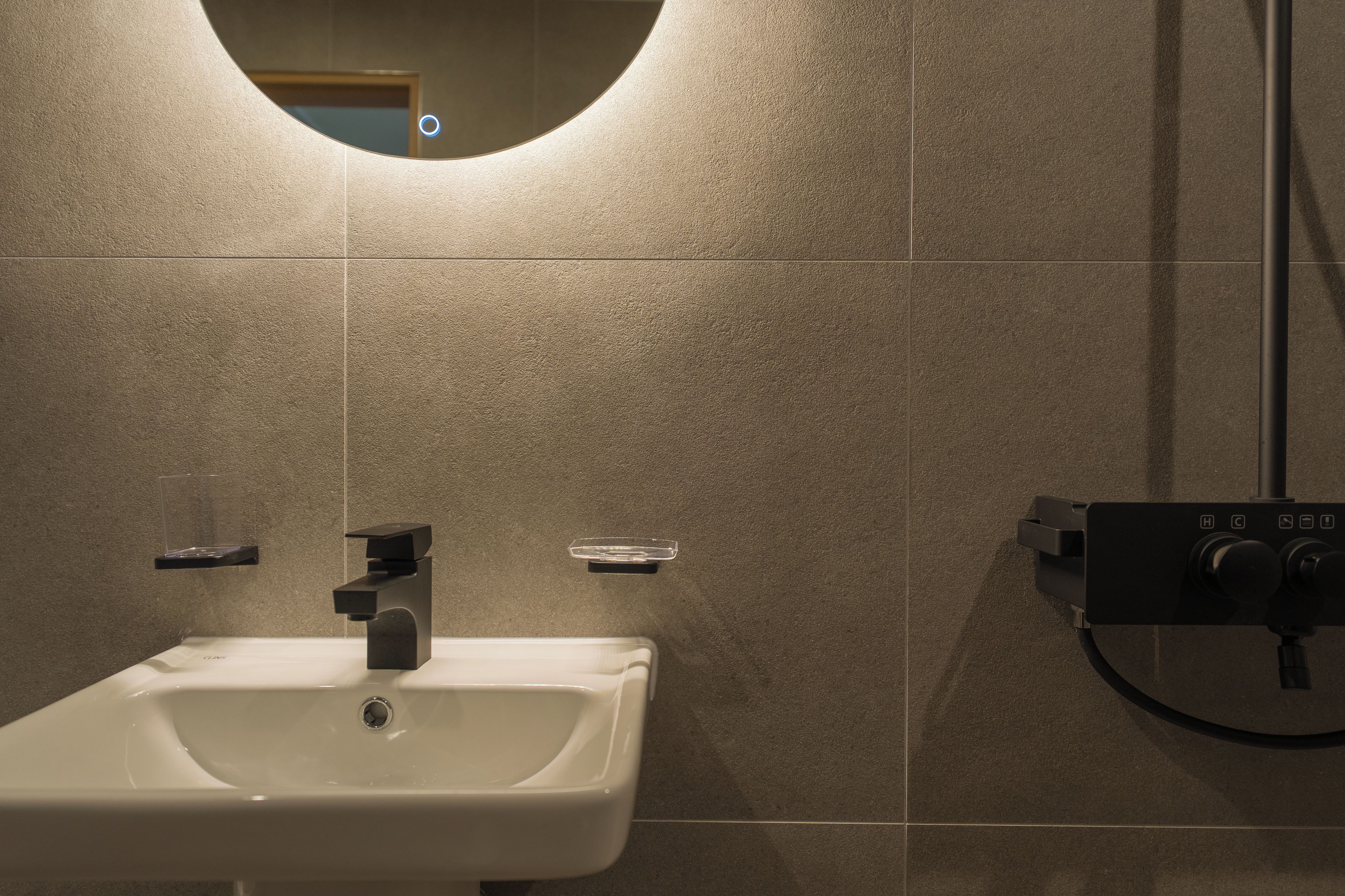 A bathroom with a white sink, a mirror, and a shower control panel.