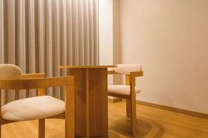 A modern room with a wooden table and two chairs, a large window with vertical blinds, and a wooden floor.
