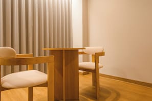 A modern room with a wooden table and two chairs, a large window with vertical blinds, and a wooden floor.