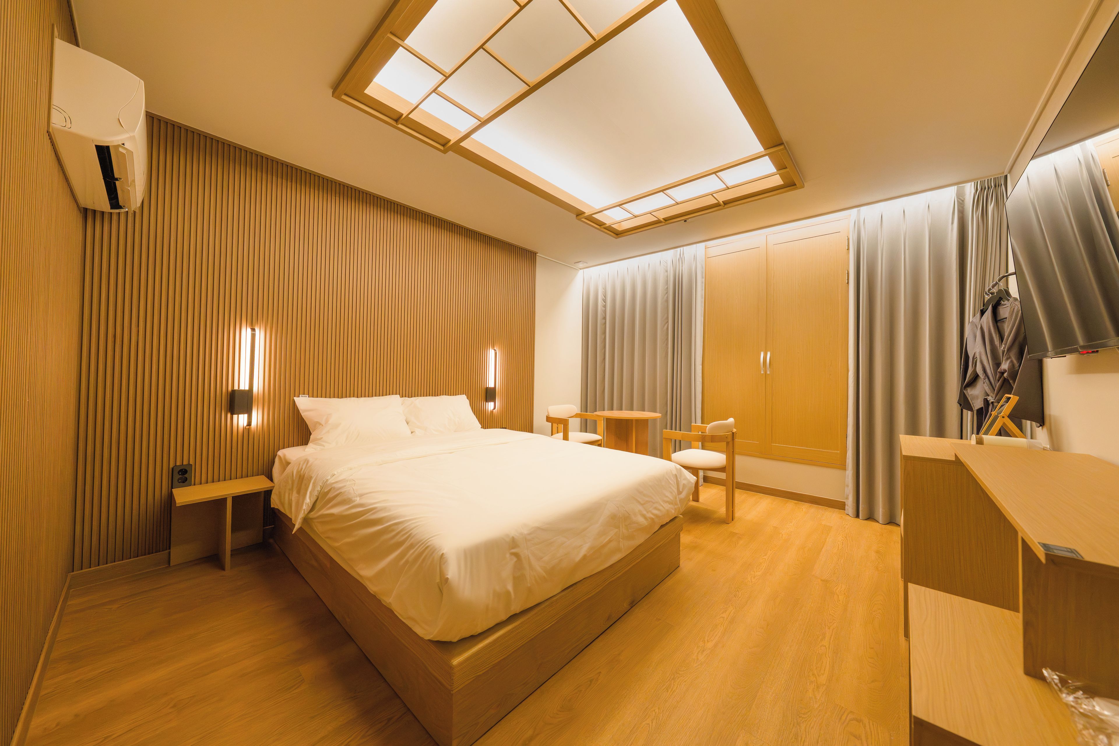 A hotel room with a large bed, a desk, a chair, a wardrobe, and a skylight.