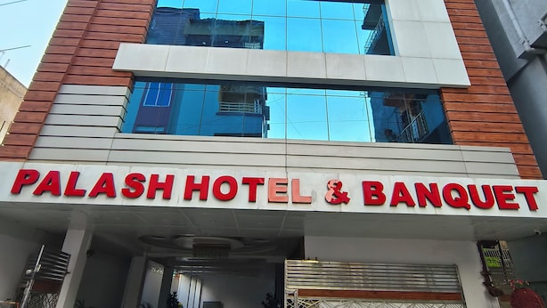 Un hotel con fachada moderna, amplias ventanas y un cartel llamativo que dice 'PALASH HOTEL & BANQUET'.
