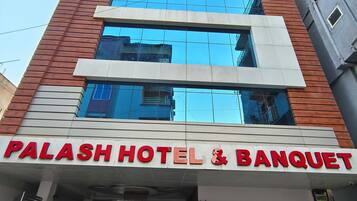 Um hotel com fachada moderna, grandes janelas e uma placa destacada com a inscrição 'PALASH HOTEL & BANQUET'.