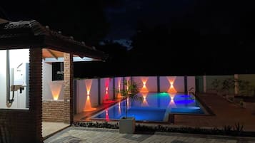 Piscina com design luminoso geométrico, estrutura de tijolo e pequena área de jardim.