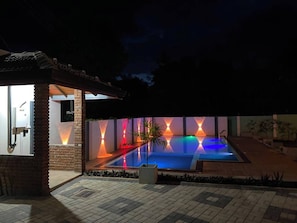 Een zwembad met een geometrisch lichtontwerp, een bakstenen constructie en een kleine tuin.