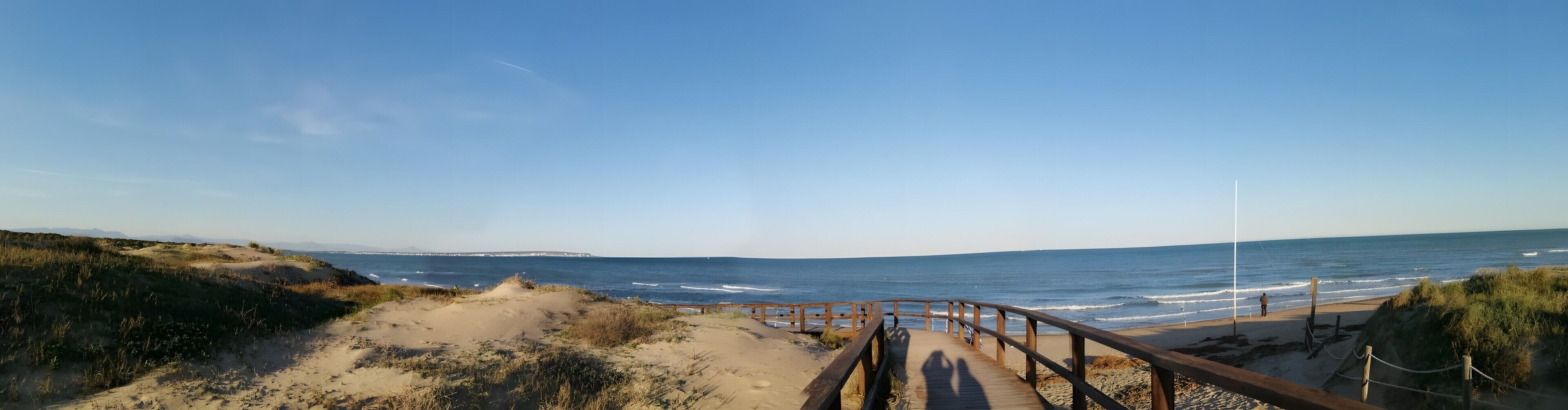 En träpromenad som leder till en strand med fri utsikt över havet och landskapet i fjärran.