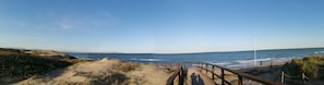 A wooden boardwalk leading to a beach with a clear view of the ocean and distant landforms.