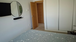 A bedroom with a bed, a wardrobe, a mirror, and a door leading to another room.