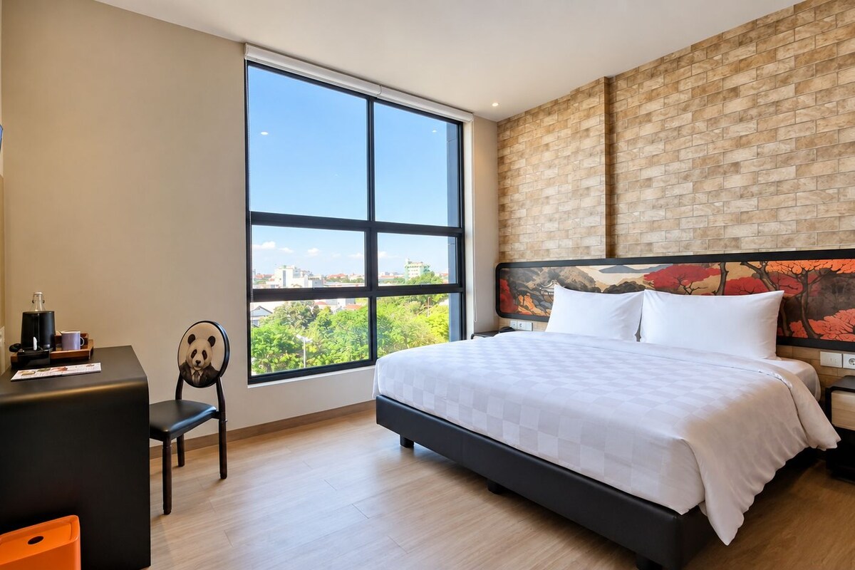 Habitación de hotel moderna con una cama grande, un escritorio, una silla y un ventanal con vistas a la ciudad.