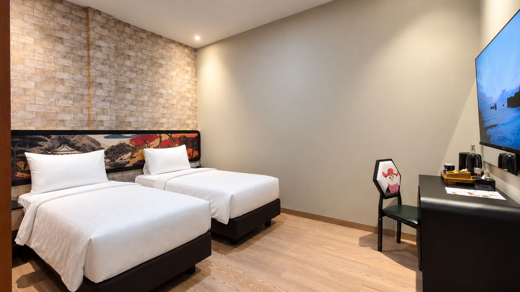 Habitación de hotel con dos camas, pared de ladrillo decorativa, televisor de pantalla plana y escritorio con silla.