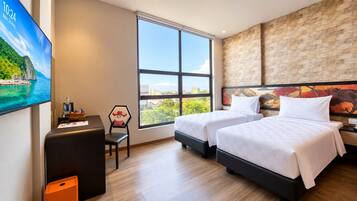 Habitación de hotel con dos camas, un escritorio con silla, un televisor y un ventanal con vistas a la ciudad.