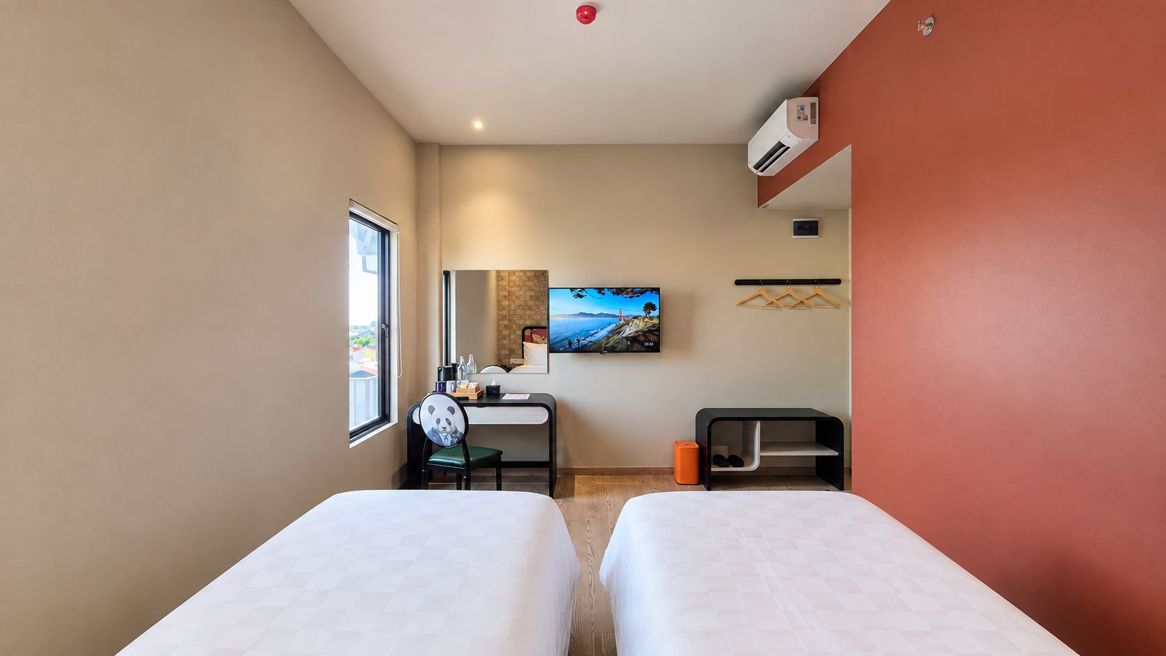 Habitación de hotel con dos camas, un escritorio con silla, un televisor montado en la pared y una ventana.